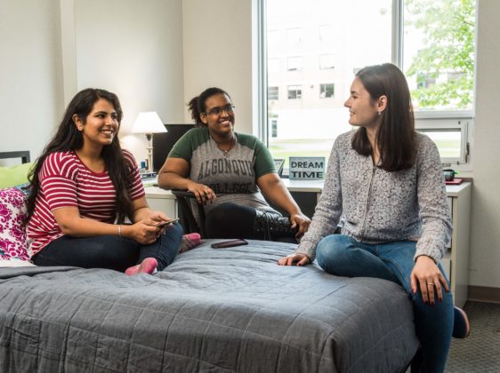 three students sitting on bed talking