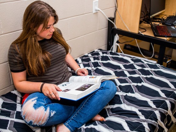 student sitting on bed reading