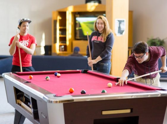 Student residence games room with pool table and three people playing pool