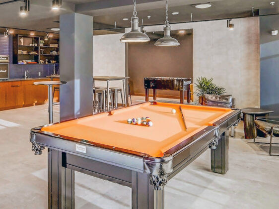 Games lounge with orange felted pool table, high top bar tables, and industrial style.